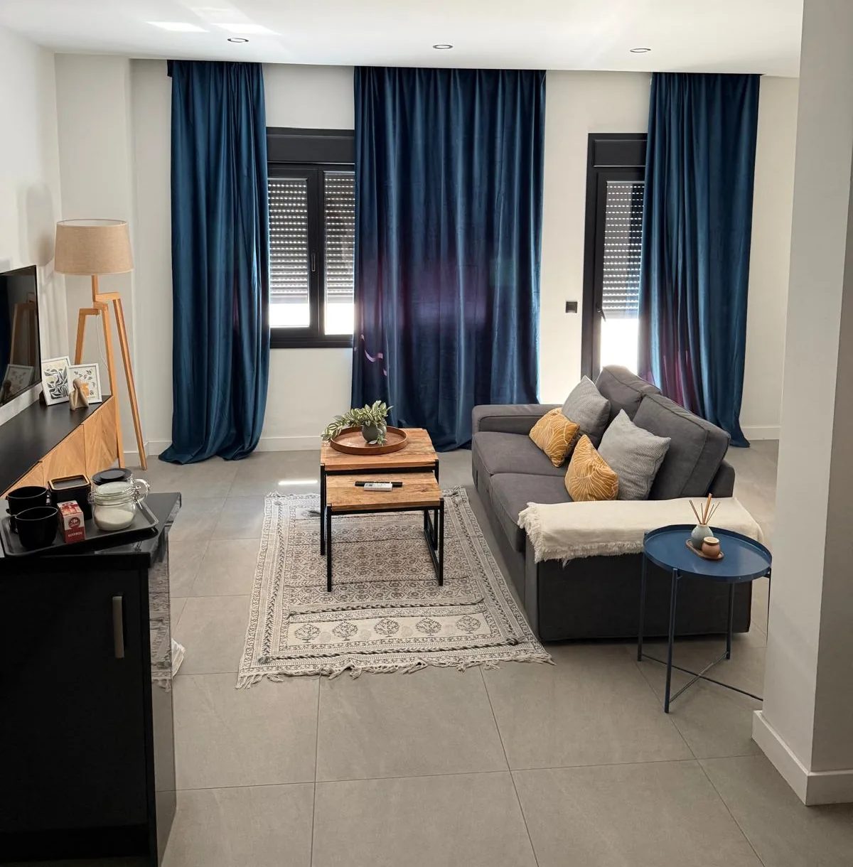 Salon w mieszkaniu: szara sofa, drewniany stolik i granatowe zasłony